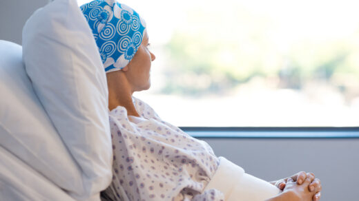 Young woman in bed suffering from cancer. Thoughtful woman battling with tumor looking out of window. Young patient with blue headscarf recovery in hospital on bed.